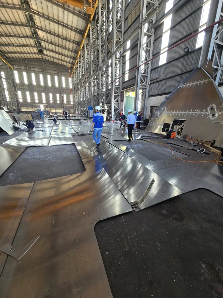 Portrait-oriented shipyard photograph of curved aluminum fabrication pieces
