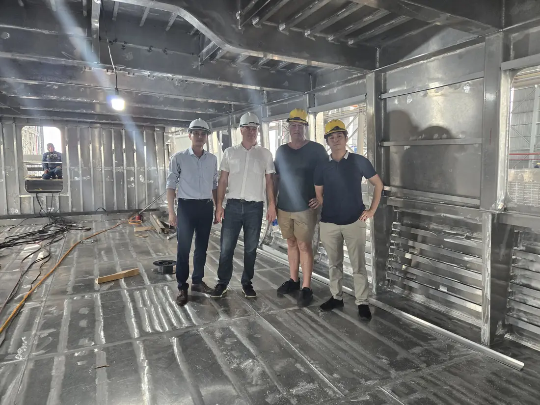 Four people inside the raw aluminum structure of a yacht under construction